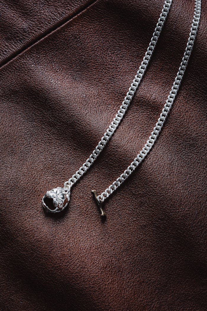 Close-up of a silver chain necklace on textured leather, showcasing intricate pendant design.