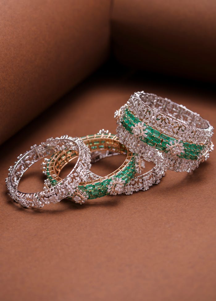Close-up of luxurious diamond and emerald bangle bracelets on brown background, exuding elegance.